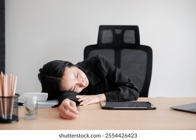 Tired businesswoman in black attire resting on desk with digital tablet and office supplies, conveying workplace fatigue. - Powered by Shutterstock