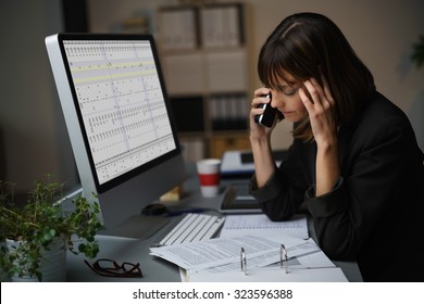 Tired Businesswoman Talking To A Client By Mobile Phone While Working On Computer And Some Business Documents.