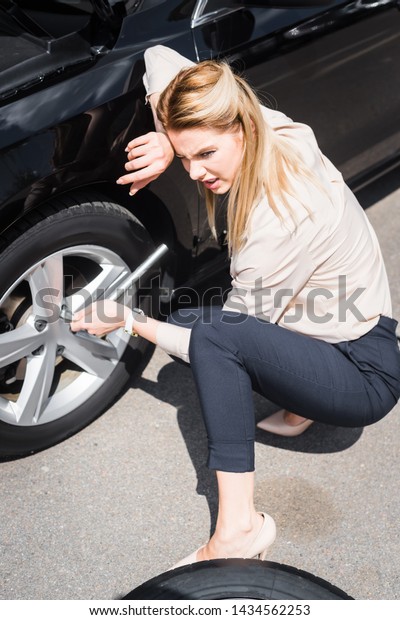 tired businesswoman with tool in hand\
sitting near broken auto, car insurance\
concept