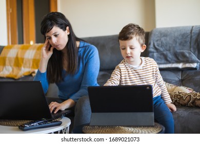 Tired Busy Woman Working On Laptop At Home With Her Child. Single Mother Telecommuting Stress. Child Using Digital Tablet While Her Mon Works.