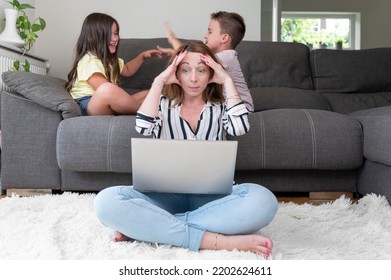 Tired Busy Woman Working On Laptop At Home With Her Children. Single Mother Telecommuting Stress. High Quality Photography.