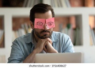 Tired Caucasian male employee put stickers with eyes painter feel fatigue exhaustion at workplace. Exhausted man worker sleep or take nap in office, overwhelmed with job. Overtime concept. - Shutterstock ID 1916408627