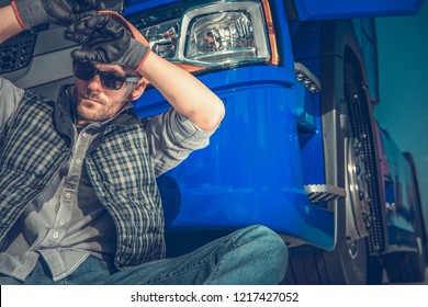Tired Caucasian Truck Driver in His 30s Resting in Front of His Semi Tractor. Transportation Industry Concept.