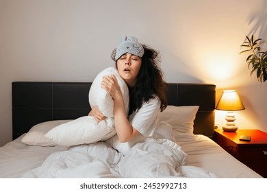 Tired Caucasian woman wearing sleep mask sitting in bed with pillow and can't sleep. Concept of insomnia and sleepless. - Powered by Shutterstock