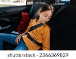 Tired child girl sleeping in car while going home from school, sitting on back seat, wearing a seat belt. Childhood, family lifestyle and safety in car concept