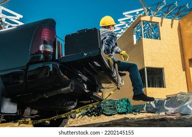 Tired Contractor Sitting On His Pickup Truck Cargo Bed Taking A Moment Of Rest During Hard Day At Work. Construction Site In The Background. Industrial Theme.