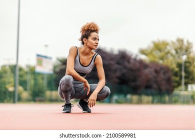 A tired, dedicated runner crouching on the trail in the stadium and taking a short break after running. A runner resting.