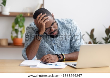 Tired depressed bored african businessman frustrated by business failure bankruptcy looking at laptop feel exhausted having headache, upset stressed black office worker worried about problem at work