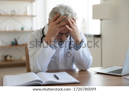 Tired depressed old male doctor feels desperate thinking of medical problem feels burnout at work. Worried upset senior physician regrets medical malpractice suffers from guilt sits alone in office.