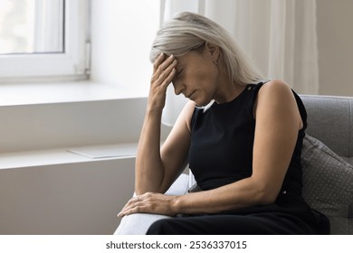 Tired depressed older woman pensioner hold hand on forehead feel headache weakness anxiety psychological discomfort. Stressed nervous aged female sit on couch with eyes closed get sudden panic attack