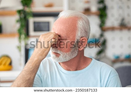 Tired, depressed senior man sitting on couch in living room feeling hurt and lonely. Aged, white-haired man touching forehead suffering from severe headache or recalling bad memories