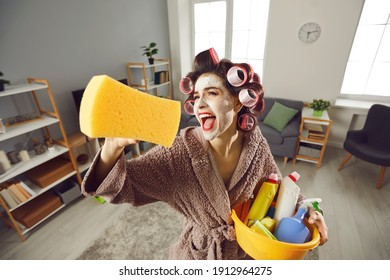 Tired desperate housewife holding yellow sponge and screaming like crazy while cleaning house. Funny young woman in hair rollers and beauty skin care face mask tidying up home, singing and having fun - Powered by Shutterstock