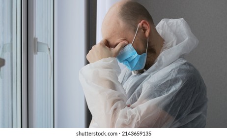 A tired doctor, after a shift in the infectious diseases department with coronovirus patients, stands at the window in the rest room, the doctor is dressed in a protective suit and mask.