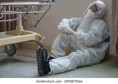 Tired Doctor Wearing Ppe Suit Take A Break Near Bed After Hard Work Feeling Worry And Sad  In Operating Room At Hospital. Exhausted And Desperate  Surgeon Of Coronavirus Pandemic  Of Covid 19 Outbreak