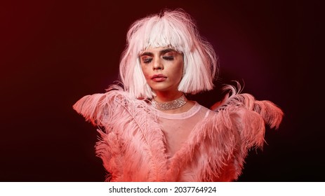 Tired Drag Queen, Young Transgender With Rubbed Bright Night Makeup Wearing Boa Feather Party Dress And White Wig, Posing Isolated In Red Neon Light Background. Lgbtqi, Drag Show Concept