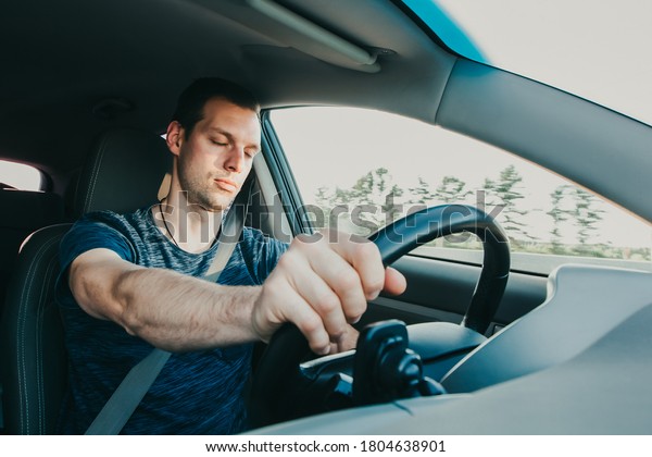 Tired driver falls\
asleep while driving car. Sleepy man wearing seat belt in vehicle.\
Risk of accident due to alcoholic intoxication. Unsafe driving from\
fatigue or drunkenness.