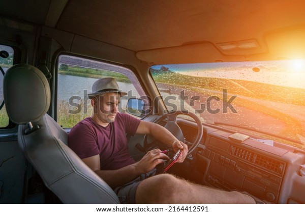Tired driver wearing hat resting\
after work inside of truck cabin with digital tablet in\
hands