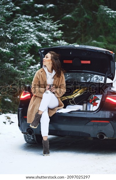 Tired driver woman\
stopped her car in winter forest road to give herself rest and to\
drink a cup of coffee