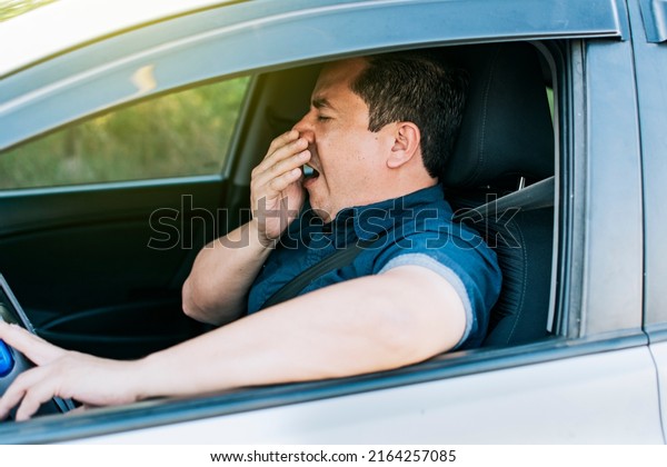 Tired\
driver yawning, concept of man yawning while driving. A sleepy\
driver at the wheel, a tired person while\
driving