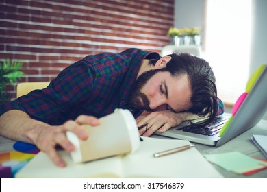 Tired editor holding disposable cup while sleeping on office desk
