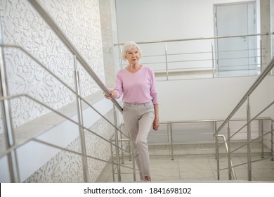 Tired. Elderly woman in a pink shirt slowly going upstairs - Powered by Shutterstock