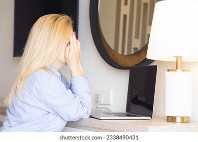 Tired european blonde business woman working on a laptop in her home office Covering her face with her hands and crying. The concept of negative remote work, freelancer no luck.