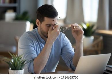 Tired exhausted businessman massaging nose bridge, taking off glasses, feeling eyestrain, sitting at work desk, young man suffering from dry eye syndrome, fatigue after long laptop use - Powered by Shutterstock