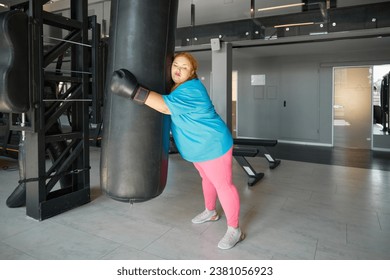 Tired exhausted fat woman leaning and hugging punching bag while training in gym - Powered by Shutterstock