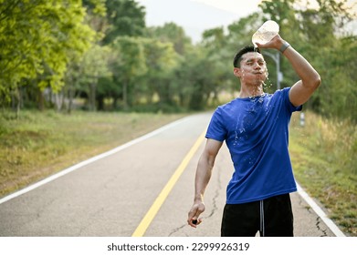 Tired and exhausted millennial Asian male runner pouring water from a bottle on his face, refreshing himself with water while running in a park. - Powered by Shutterstock