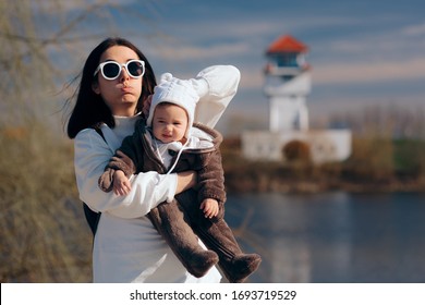 Tired Exhausted Millennial Mom Carrying Baby Girl. Overprotective Mother Arranging Baby Hat In Windy Weather
