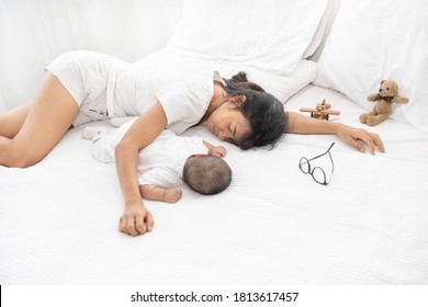 Tired Exhausted Mother Sleeping Sleep With Baby On White Bed. Overwhelmed New Asian Mom Feeling Sleep Deprived And Fatigued With Infant At Bedroom.