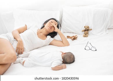 Tired Exhausted Mother Sleeping Sleep With Baby On White Bed. Overwhelmed new asian mom feeling sleep deprived and fatigued with infant at bedroom.