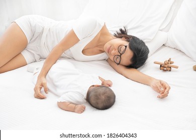 Tired Exhausted Mother Sleeping Sleep With Baby On White Bed. Overwhelmed New Asian Mom Feeling Sleep Deprived And Fatigued With Infant At Bedroom.