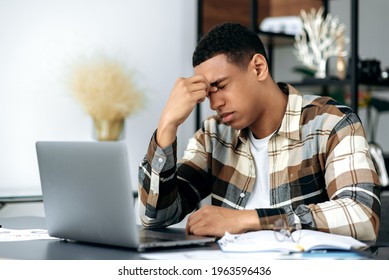 Tired Exhausted Successful Mixed Race Latino Male Freelancer Or Office Employee, Sits At Work Desk With Closed Eyes, Rubs His Eyes, Feeling Headache, Stress And Fatigue From Overtime Work, Need Rest