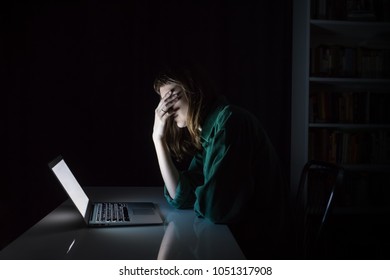 Tired And Exhausted Young Woman Hides Eyes With Hand At Laptop Pc Late In The Evening. Portrait Of Depressed Female Student Or Worker Sitting In Front Of Computer Screen At Night, Concept Of Anxiety