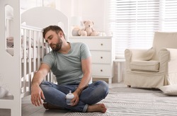 Tired Father With Bottle Of Milk Sleeping On Floor In Children's Room