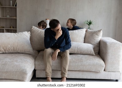 Tired Father Suffering From Headache, Feeling Annoyed And Exhausted By Noisy Kids Running Around, Frustrated Dad Sitting On Couch In Living Room, Having Problem With Naughty Active Children