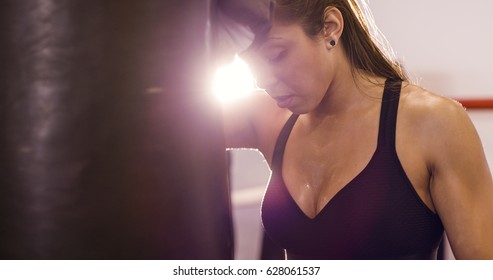 Tired female boxer resting with her arms on the punching bag - Powered by Shutterstock