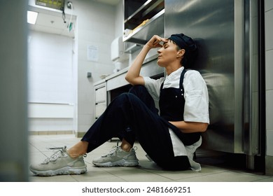 Tired female cook relaxing on the floor while working in restaurant. Copy space.  - Powered by Shutterstock