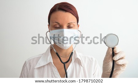 A tired female doctor with a medical mask over her face, holding a stethoscope in her hand. The female doctor fell asleep doing her job.