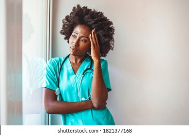Tired female doctor near window in her office. Closeup portrait sad health care professional with headache, stressed, holding head against window glass.