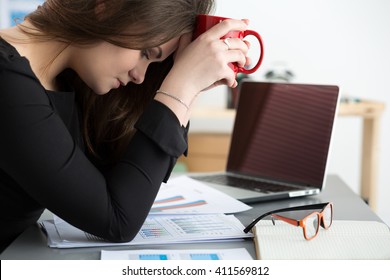 Tired Female Employee At Workplace In Office Holding Cup Of Tea. Sleepy Worker Early In The Morning After Late Night Work. Overworking, Making Mistake, Stress, Termination Or Depression Concept