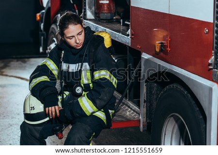 tired female firefighter in uniform with helmet sitting on truck at fire station