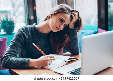 Tired female graphic designer creating new sketches using modern laptop computer and textbook, worried hipster girl learning languages online and installing application via new netbook indoors - Powered by Shutterstock