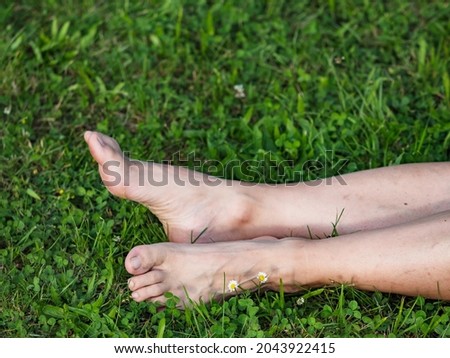 Tired female legs with bare feet on the green grass. Mature woman lays in short fresh green grass.