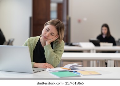 Tired female mature student falling asleep during boring online lesson, sleepy bored middle-aged woman getting second education sitting at desk with laptop in university library, selective focus - Powered by Shutterstock