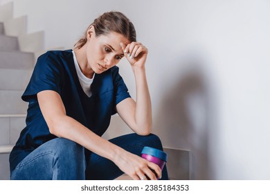 Tired female medical worker doctor holding cup of coffee taking pause in work. Exhausted nurse surgeon assistant having break after surgery, difficult medical case, patient`s death - Powered by Shutterstock