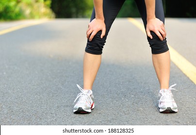 Tired Female Runner Taking A Rest After Running Hard In Countryside Road. Sweaty Athlete After Marathon Training In Country Road. 