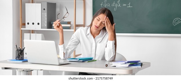 Tired Female Teacher Checking Homework In Classroom