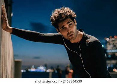 Tired fit man dressed in tracksuit listening audio music in earphones leaning against the wall during break after hard evening workout.Exhausted male jogger in active wear after sport training outdoor - Powered by Shutterstock